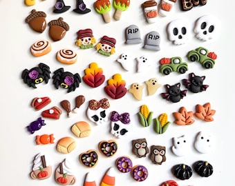 Könnte beinhalten: Eine Sammlung kleiner Ohrstecker aus Polymer-Ton mit verschiedenen Herbst- und Halloween-Motiven, darunter Kürbisse, Geister, Totenköpfe, Spinnen, Fledermäuse, Zuckermais, Blätter, Eicheln, Truthähne, Eulen und saisonale Leckereien.