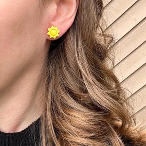 Puede incluir: Un par de pendientes de bot&oacute;n de sol amarillo. Los pendientes son peque&ntilde;os y simples, con un dise&ntilde;o de sol amarillo brillante.