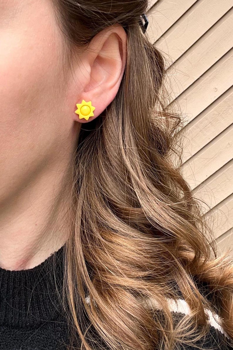 Puede incluir: Un par de pendientes de bot&oacute;n de sol amarillo. Los pendientes son peque&ntilde;os y simples, con un dise&ntilde;o de sol amarillo brillante.