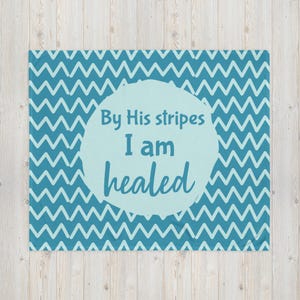 Puede incluir: Una manta turquesa con un patrón de zigzag repetido. El centro presenta un círculo azul claro con las palabras "By His stripes I am healed" en escritura turquesa.