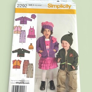 May include: Simplicity sewing pattern 2292 for children's clothing. The pattern includes designs for jackets, skirts, pants, and hats. The package features images of children wearing the finished garments. The size is A, for sizes 1/2, 1, 2, 3, and 4.