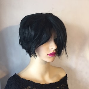May include: A black short bob wig with choppy layers and side-swept bangs. The wig is styled on a mannequin head.