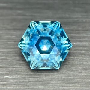 May include: A faceted blue gemstone with a hexagonal shape and a star-like pattern in the center.