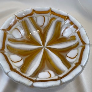 May include: A white and amber glass bowl with a swirling pattern. The bowl is made of individual pieces of glass that have been fused together.