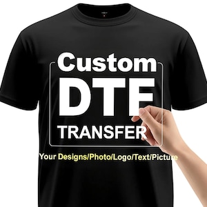 May include: Black t-shirt with white text that reads "Custom DTF TRANSFER" inside a white rectangle. Below the rectangle is the text "Your Designs/Photo/Logo/Text/Picture".