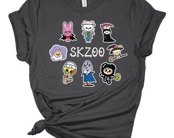 May include: Dark gray t-shirt featuring a colorful graphic of cartoon characters with the text "SKZOO". The graphic includes various characters in Halloween costumes. The shirt is made of a soft material.