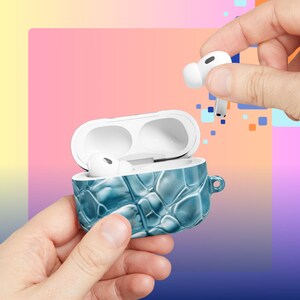 May include: A blue textured case for wireless earbuds, held open to reveal the white earbuds inside. One earbud is being held above the case. The case has a small loop on the side.