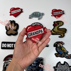 May include: A collection of embroidered iron-on patches featuring various designs, including a heart with the text "Grandpa", a paw print, a snake, a turtle, a parrot, a panther, a bulldog, and a text patch that says "Do Not Disturb".