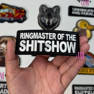 May include: A collection of embroidered patches with various designs and text. One patch reads "RINGMASTER OF THE SHITSHOW" in white lettering on a black background. Other patches feature a wolf, a horse, and a fire truck.
