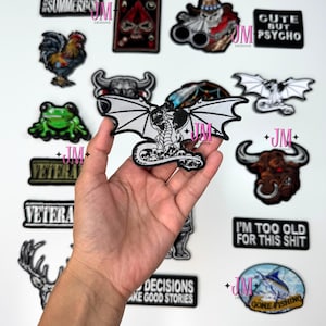 Pode incluir: Uma coleção de patches bordados para passar a ferro com vários designs, incluindo uma caveira, um galo, um dragão, um touro, um sapo, um peixe e texto. Os patches são todos em preto e branco com alguns acentos de cor.