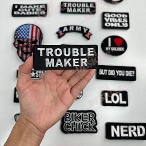 May include: A collection of iron-on patches with various designs and text, including "Trouble Maker", "Biker Chick", "Nerd", "Biker Babe", "Good Vibes Only", "Army", "I Love My Soldier", "But Did You Die?", "LOL", "I Make Cute Babies", "#NoFilter", "No Thanks", and a skull with an American flag design.