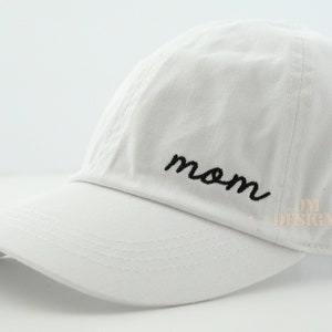 May include: White baseball cap with a black embroidered "mom" on the front.