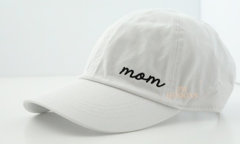May include: White baseball cap with a black embroidered "mom" on the front.