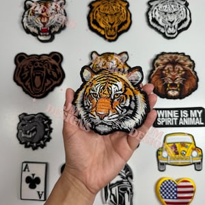 May include: A collection of embroidered patches featuring animal faces, including tigers, a bear, a lion, and a bulldog. Other patches include a playing card, a car, a heart with an American flag design, and a patch with the text "WINE IS MY SPIRIT ANIMAL."