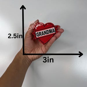 May include: A red heart-shaped patch with the word "GRANDMA" in white lettering. The patch is approximately 3 inches wide and 2.5 inches tall. The design features a classic tattoo style with a black outline.