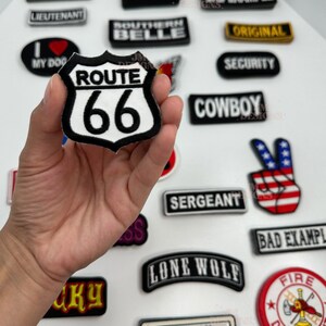 May include: A collection of embroidered patches with various designs and text. One patch features the text "ROUTE 66" in a white and black shield shape. Other patches include "OLD SKOOL", "SEXY", and "BAD EXAMPLE".