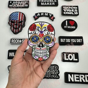 May include: A collection of embroidered iron-on patches featuring various designs and phrases, including "#NOFILTER", "NO THANKS", "TROUBLE MAKER", "I MAKE CUTE BABIES", "ARMY", "GOOD VIBES ONLY", "MY SOLDIER", "ROCKS", "BUT DID YOU DIE?", "LOL", "NERD", "BIKER BABE", and a colorful sugar skull design.