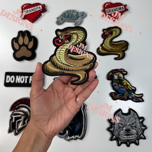 Peut inclure: Une collection de patchs brodés thermocollants avec différents motifs, dont un serpent, une empreinte de patte, une tortue, un perroquet, un chien, un casque et deux cœurs avec les mots "Grand-mère" et "Grand-père".