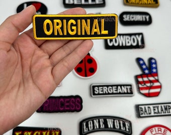 May include: A collection of embroidered iron-on patches with various designs and text, including "Original", "Cowboy", "Lucky", "Lone Wolf", "Fire Department", "Route 66", "Old Skool", "Sergeant", "Princess", "Southern Belle", "Bad Example", "Security", "Sexy", "Lieutenant", and "Old Skool".