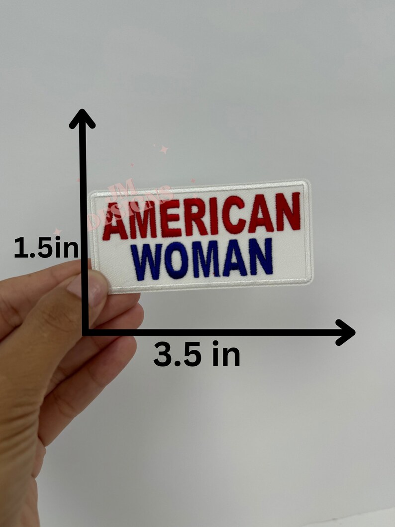 May include: White iron-on patch with red and blue embroidered text that reads "AMERICAN WOMAN". The patch measures 3.5 inches wide and 1.5 inches tall.