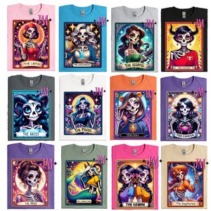 May include: Twelve t-shirts featuring a colorful illustration of a Day of the Dead-inspired tarot card for each zodiac sign. The shirts are in various colors, including pink, blue, gray, white, orange, purple, and beige.