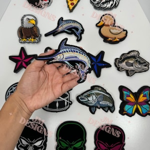 Peut inclure: Une collection de patchs brodés thermocollants avec différents motifs, dont un crâne, un loup, un poisson, un papillon, une part de pizza, une batterie, une étoile, un canard, un aigle et un marlin.