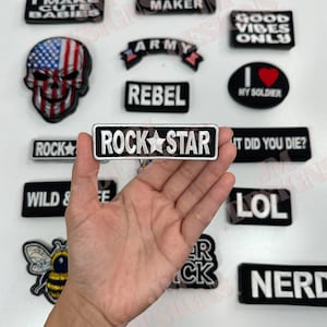 May include: A collection of embroidered iron-on patches with various designs and text, including "Rockstar", "Rebel", "Good Vibes Only", "I Love My Soldier", "Wild & Free", "Nerd", "Biker Babe", and "Trouble Maker".