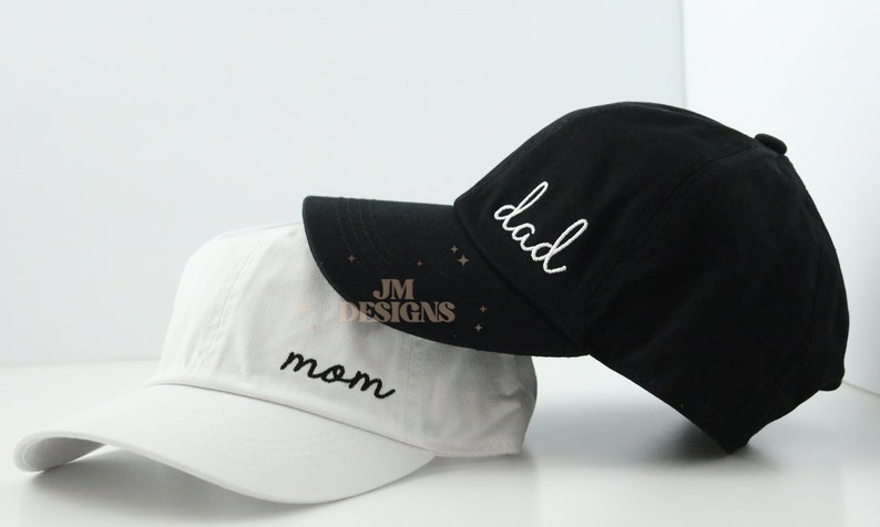 May include: Two baseball caps, one white with "mom" embroidered in black and one black with "dad" embroidered in white.