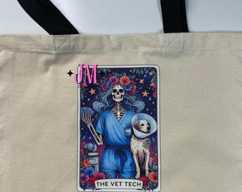 Puede incluir: Bolso tote beige con asas negras, con un gráfico colorido. El gráfico muestra un esqueleto con uniforme azul con un perro con collar isabelino, rodeado de flores y estrellas. El texto dice "THE VET TECH."