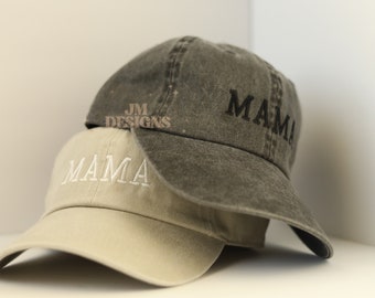 May include: Two baseball caps, one in beige with white embroidery that says "MAMA" and one in dark gray with black embroidery that says "MAMI".