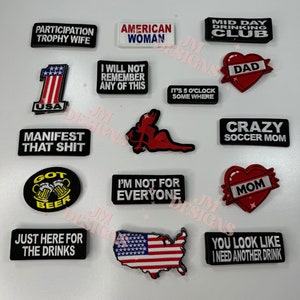 May include: A collection of 14 iron-on patches with various designs and sayings. The patches are mostly white, black, red, and blue. Some of the sayings include "Participation Trophy Wife", "American Woman", "I Will Not Remember Any Of This", "Manifest That Shit", "Got Beer", "I'm Not For Everyone", "Just Here For The Drinks", "Mid Day Drinking Club", "Dad", "It's 5 O'Clock Somewhere", "Crazy Soccer Mom", "Mom", and "You Look Like I Need Another Drink".