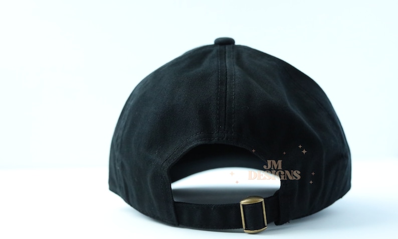 May include: Black baseball cap with an adjustable strap and a small gold logo that says "JM DESIGNS" on the back.
