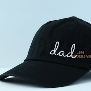 May include: Black baseball cap with white embroidery that says "dad" and a small brown logo that says "JM DESIGNS".