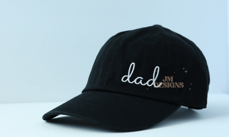 May include: Black baseball cap with white embroidery that says "dad" and a small brown logo that says "JM DESIGNS".