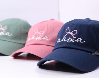 May include: Three baseball caps with the word "mama" embroidered in white with a pink bow above the word. The caps are in green, pink, and navy blue.