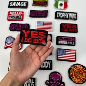 Puede incluir: Una colección de parches bordados para planchar con diferentes frases y diseños. Los parches son negros, rojos, blancos, verdes y morados. Algunas de las frases en los parches incluyen "Yes I Do Bite", "High Maintenance", "Savage", "Sweetheart", "Trophy Wife", "Warning Bombshell", "Milf", "Mexico", "Girl Bad", "Daddy" y "Fire Dept."