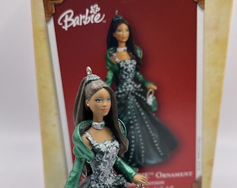 May include: A black and green Barbie doll ornament with a tiara and a necklace. The doll is wearing a long, flowing gown with a green fur shawl. The ornament is part of a Barbie Christmas ornament collection.