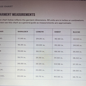 Puede incluir: Una tabla de tallas de prendas con medidas en pulgadas. La tabla muestra las medidas de hombro, largo, pecho y manga para las tallas XS a XXXL. Las medidas son aproximadas.