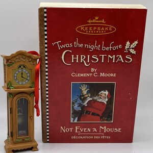 May include: A Hallmark Keepsake Ornament featuring a wooden grandfather clock with a white face and black hands. The clock is decorated with holly and a red ribbon. The ornament is packaged in a red box with the title "Twas the night before Christmas" by Clement C. Moore and the subtitle "Not Even a Mouse" in gold lettering.