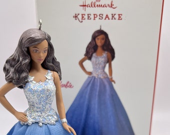 May include: Hallmark Keepsake Ornament featuring a Barbie doll wearing a blue and silver gown. The ornament is packaged in a white box with the Hallmark logo and the word "Keepsake" printed on it.