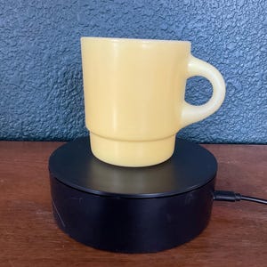 May include: A solid light yellow mug with a smooth, opaque finish and a rounded handle. The mug features a straight-sided cylindrical body with a slightly wider base, showcasing a clean, simple design without any patterns or additional text.