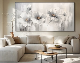 May include: A large abstract painting of white flowers on a gray background. The painting is hanging on a wall above a white sectional sofa and two coffee tables.