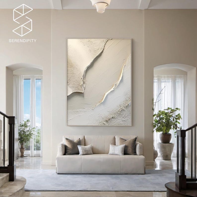 May include: A white and gold abstract painting with a textured surface. The painting is framed and hanging on a wall in a modern living room.