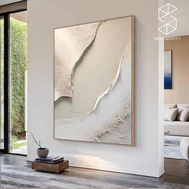 May include: Abstract wall art featuring a textured white and gold painting with a modern design. The painting is framed in a thin gold frame and is hanging on a white wall.