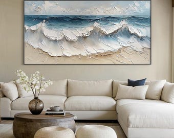May include: A painting of ocean waves crashing on a sandy beach. The waves are white and blue, and the sand is beige. The painting is framed in a black frame.