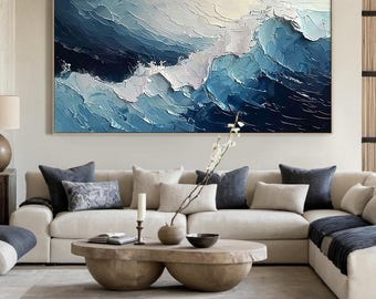 May include: Abstract painting of blue and white waves with a textured, brushstroke effect. The painting is framed and hanging on a wall above a white sectional sofa with pillows.
