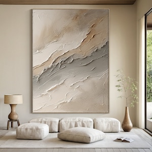 May include: Abstract painting with a textured, layered look in shades of beige, brown, and gray. The painting is framed and hanging on a wall in a modern living room.