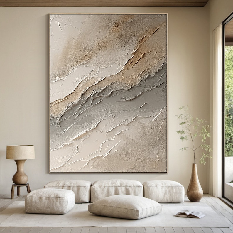 May include: Abstract painting with a textured, layered look in shades of beige, brown, and gray. The painting is framed and hanging on a wall in a modern living room.