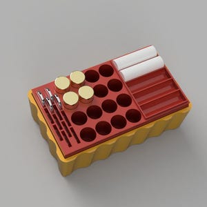 May include: A yellow and red makeup organizer with various compartments. It features round holes, rectangular slots, and a small tray. Gold-lidded jars, silver tools, and white cylindrical objects are visible.