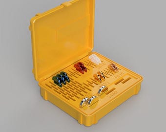 Puede incluir: Una caja de plástico amarilla, abierta para revelar varios objetos de colores y metálicos. La caja contiene varios objetos pequeños y curvos en tonos azul, rojo, blanco y dorado, junto con piezas plateadas. La caja está numerada.